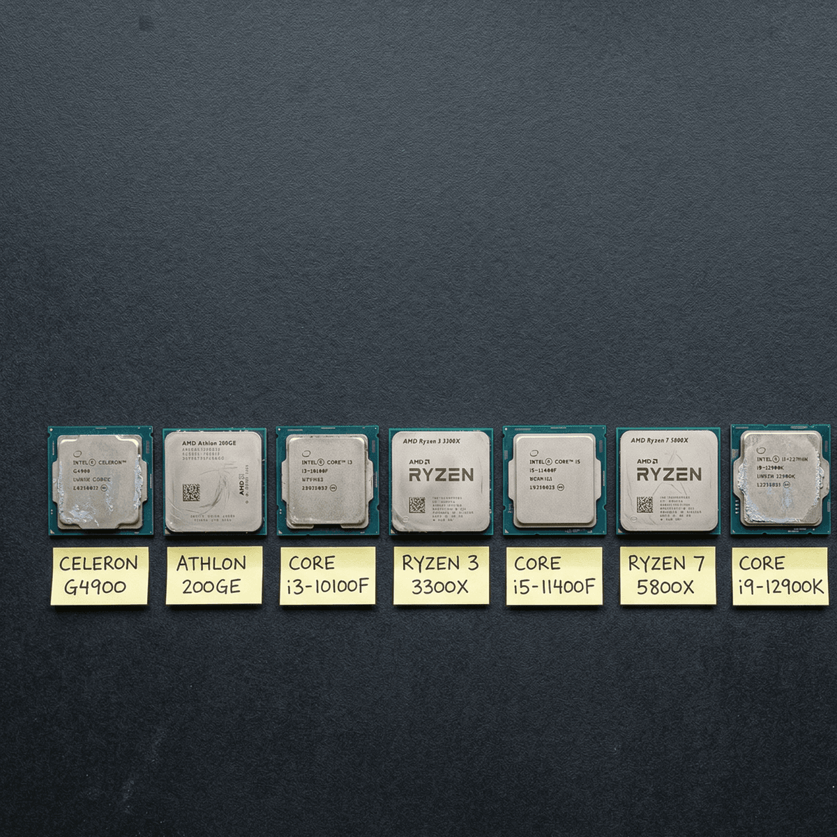Eight used AMD and Intel processors arranged in a row on a dark surface with sticky label name tags