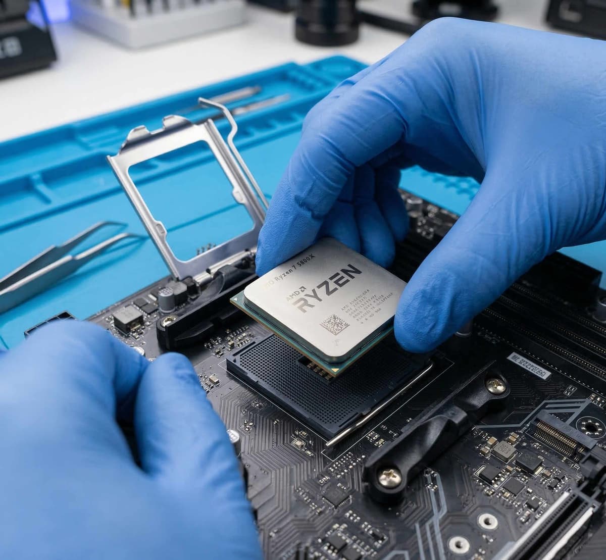 Hands installing a CPU into a motherboard socket on a clean dark desk with orange-handled tools nearby
